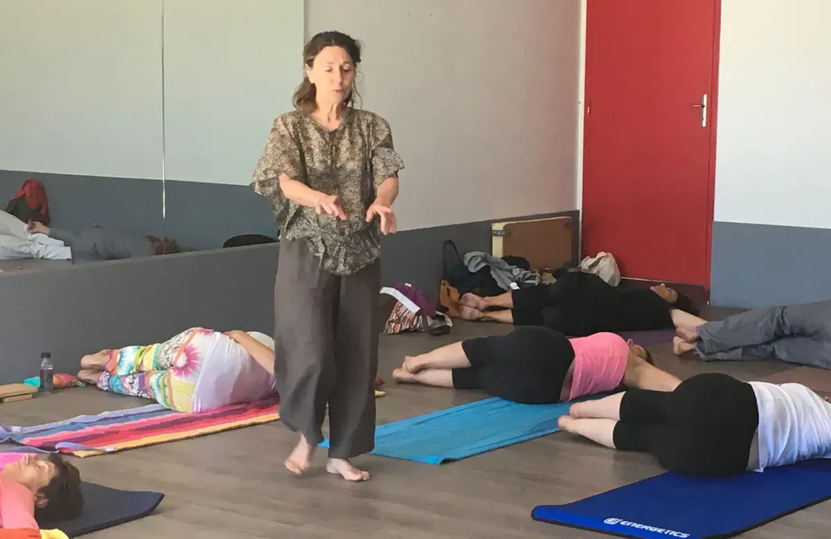 Une enseignante pieds nus guide des participants allongés sur le côté sur leurs tapis, lors d'une séance de yoga en salle