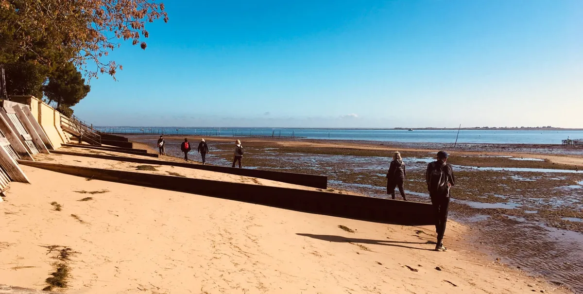 Le rivage du bassin à marée basse, une embarcation posée sur le sable et des promeneurs au loin