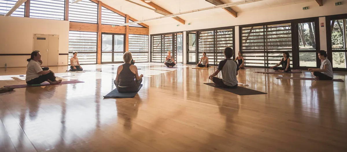 Un groupe assis sur des tapis de yoga dans une salle en bois largement vitrée